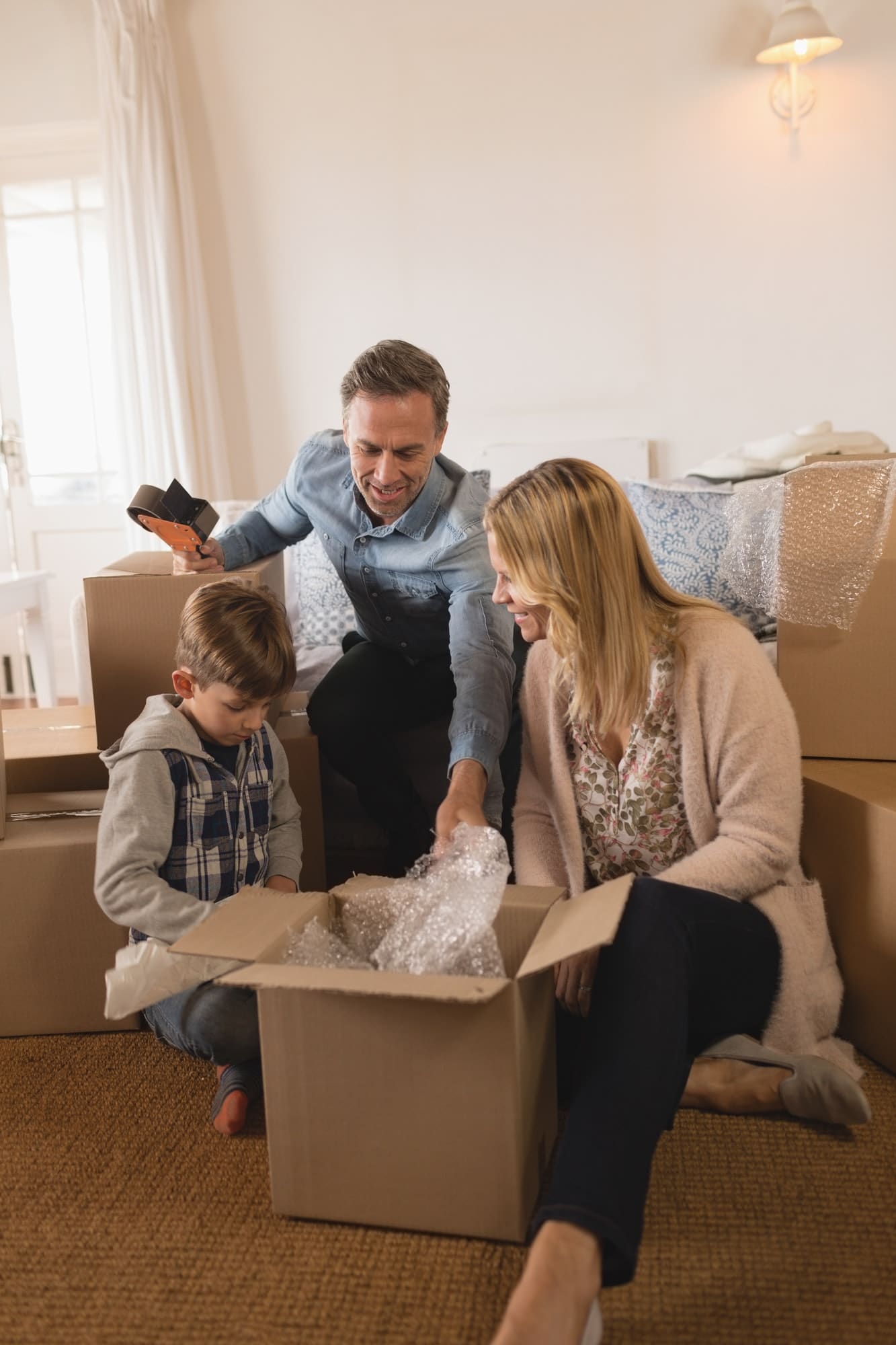 Front view of happy family in casual clothes unpacking cardboard boxes in their new home